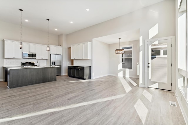 kitchen featuring stainless steel appliances, a kitchen island with sink, light countertops, and white cabinetry