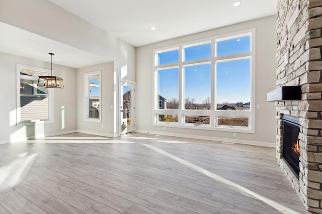 unfurnished living room with baseboards, light wood-type flooring, a fireplace, and a notable chandelier