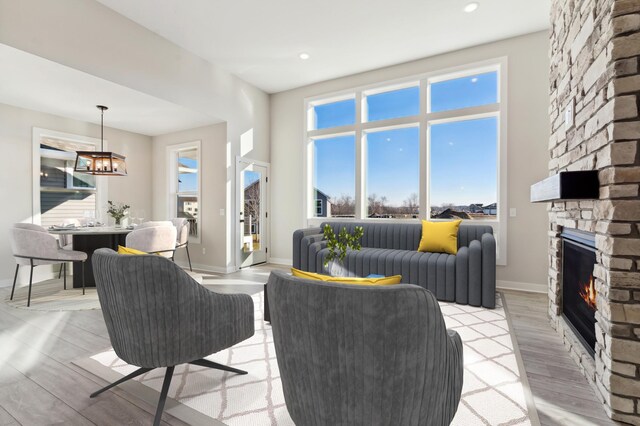 living area featuring light wood finished floors, baseboards, a high ceiling, a stone fireplace, and a chandelier