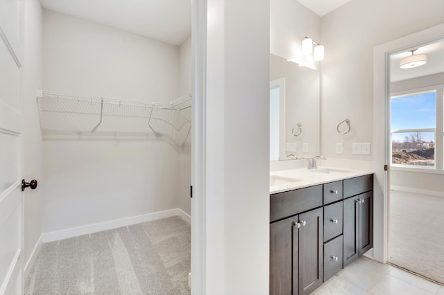 bathroom featuring double vanity, a spacious closet, baseboards, and a sink