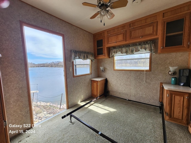 kitchen featuring a ceiling fan, glass insert cabinets, brown cabinetry, and light countertops