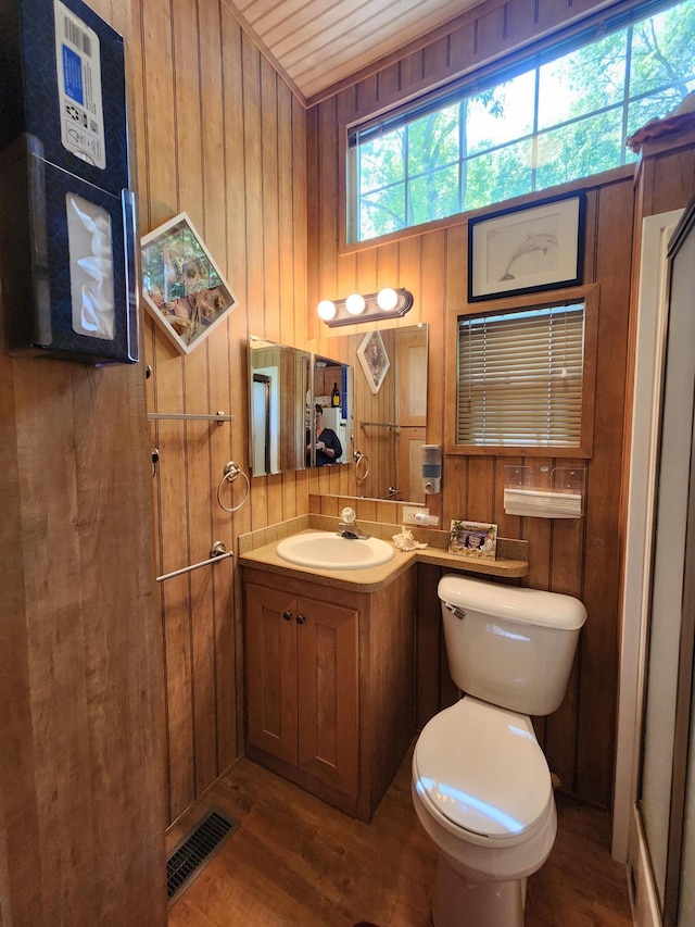 bathroom with visible vents, toilet, wooden walls, vanity, and wood finished floors