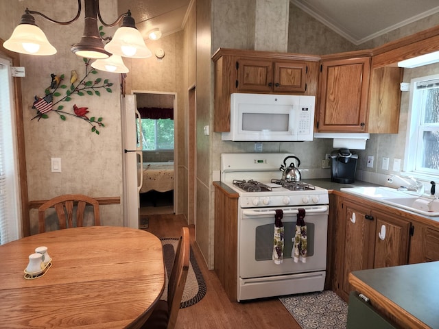 kitchen with white appliances, wood finished floors, a sink, vaulted ceiling, and crown molding