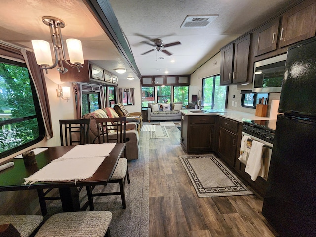 kitchen with stainless steel microwave, visible vents, gas stove, freestanding refrigerator, and dark brown cabinets