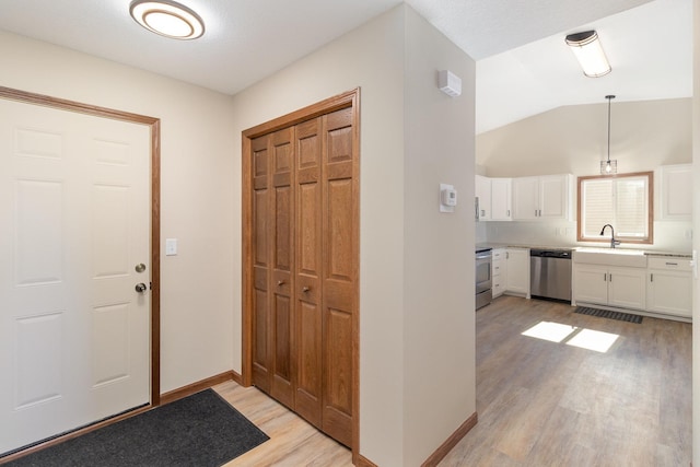 entrance foyer featuring light wood-style floors, vaulted ceiling, and baseboards