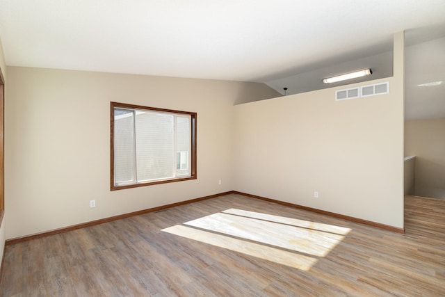 unfurnished room featuring visible vents, vaulted ceiling, light wood-style flooring, and baseboards