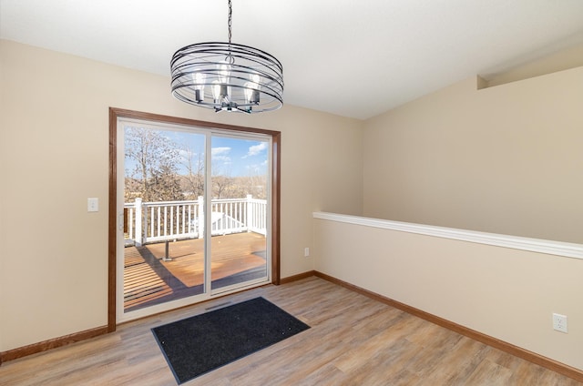 doorway featuring a chandelier, light wood-type flooring, and baseboards