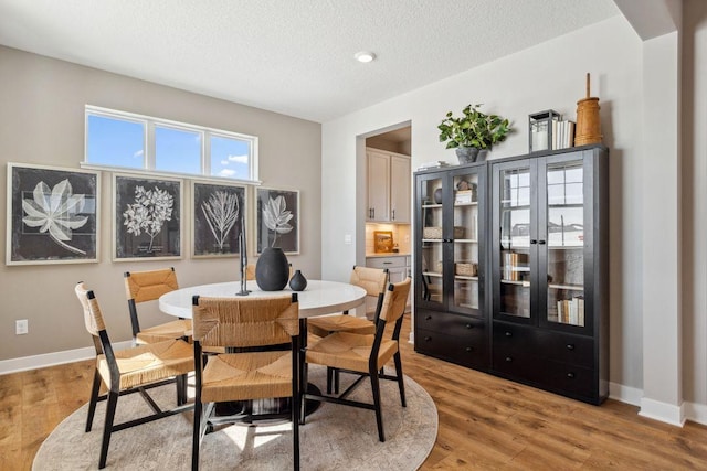 dining space featuring a textured ceiling, light wood-type flooring, and baseboards