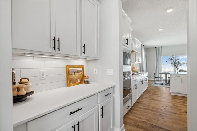 kitchen with wood finished floors, white cabinets, a textured ceiling, stainless steel oven, and backsplash