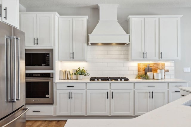 kitchen featuring custom exhaust hood, appliances with stainless steel finishes, light countertops, and white cabinetry