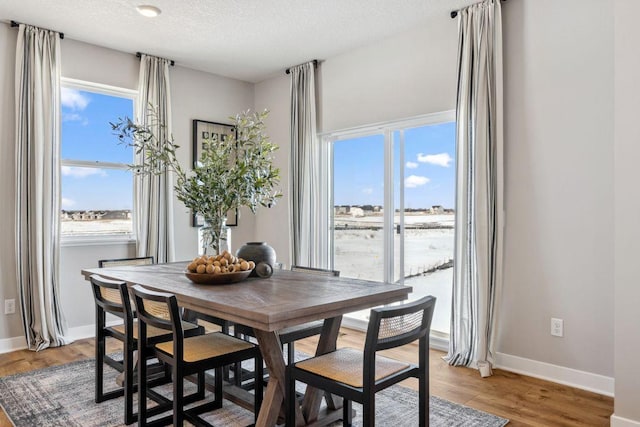 dining space with baseboards, light wood-type flooring, and a textured ceiling