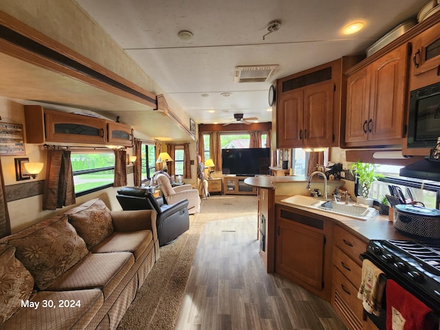 kitchen with brown cabinets, open floor plan, wood finished floors, black microwave, and a sink