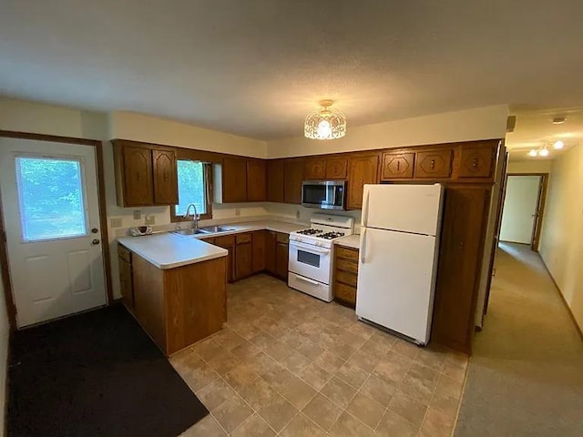 kitchen featuring white appliances, light countertops, a peninsula, and a sink