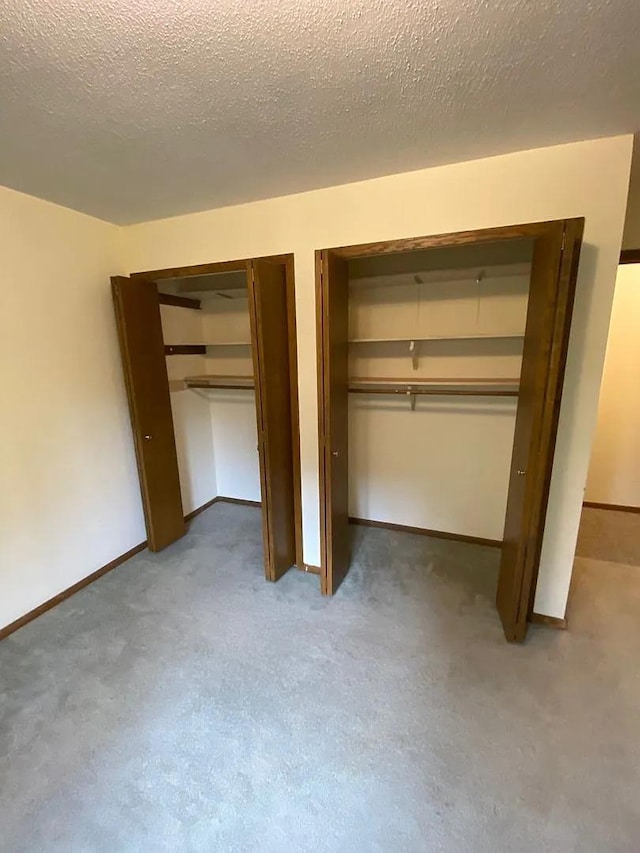 unfurnished bedroom with baseboards, multiple closets, a textured ceiling, and carpet floors