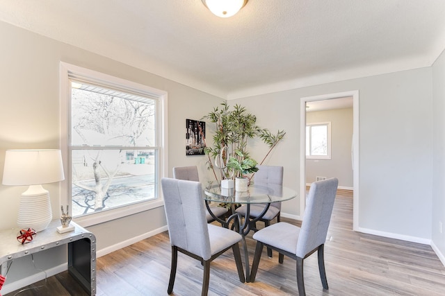 dining room with light wood-style flooring, baseboards, and a textured ceiling