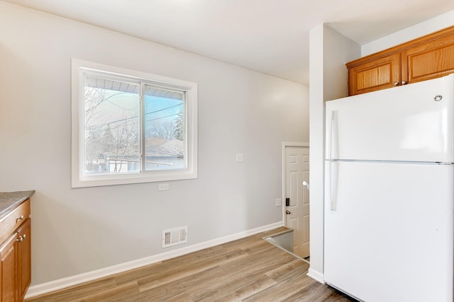 kitchen featuring visible vents, baseboards, light wood-style flooring, brown cabinets, and freestanding refrigerator