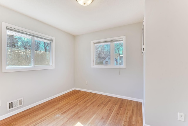 spare room with light wood finished floors, visible vents, and baseboards