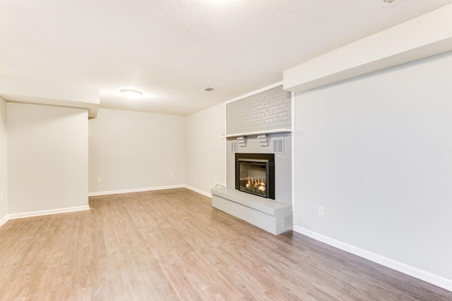 unfurnished living room with a fireplace, visible vents, light wood-style flooring, a textured ceiling, and baseboards