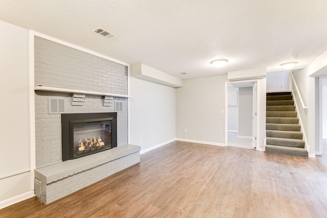 unfurnished living room featuring visible vents, stairway, wood finished floors, a textured ceiling, and a fireplace