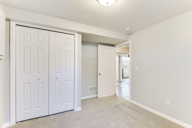 unfurnished bedroom featuring a textured ceiling, carpet floors, visible vents, baseboards, and a closet