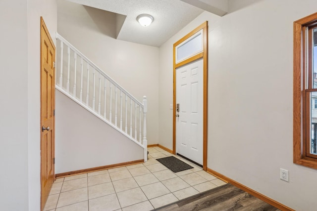 entrance foyer featuring stairs, light tile patterned floors, a textured ceiling, and baseboards