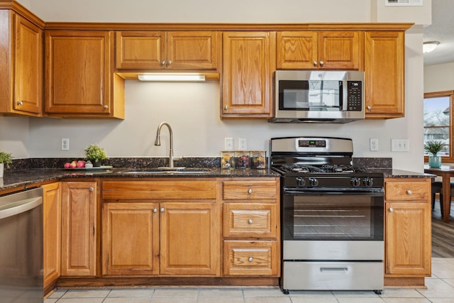 kitchen featuring appliances with stainless steel finishes, brown cabinetry, a sink, and dark stone countertops