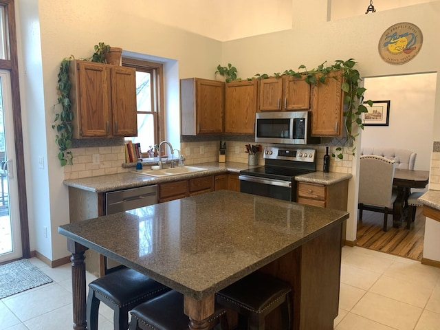 kitchen featuring brown cabinetry, a breakfast bar, a sink, stainless steel appliances, and backsplash