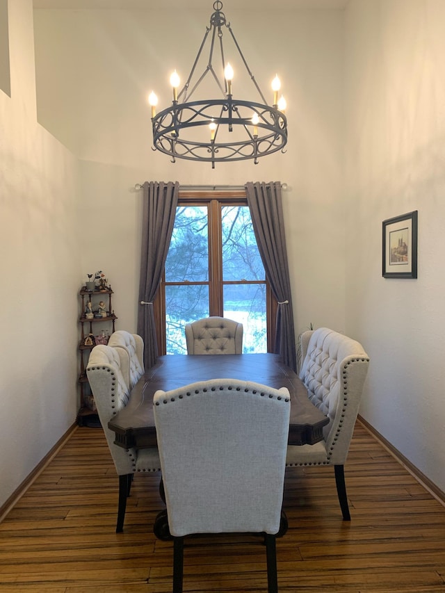 dining space featuring an inviting chandelier, a high ceiling, baseboards, and wood finished floors