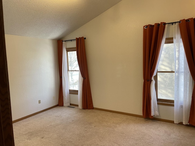 unfurnished room featuring a textured ceiling, lofted ceiling, baseboards, and light carpet