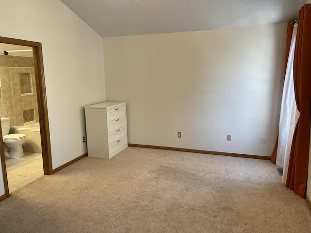 unfurnished bedroom with light carpet, connected bathroom, lofted ceiling, and baseboards