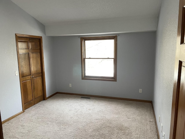 unfurnished bedroom with a closet, visible vents, light colored carpet, and baseboards