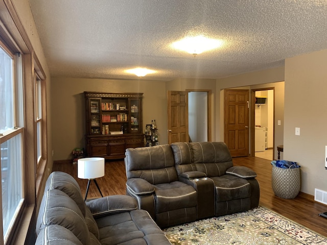 living area featuring visible vents, washer / clothes dryer, a textured ceiling, and wood finished floors