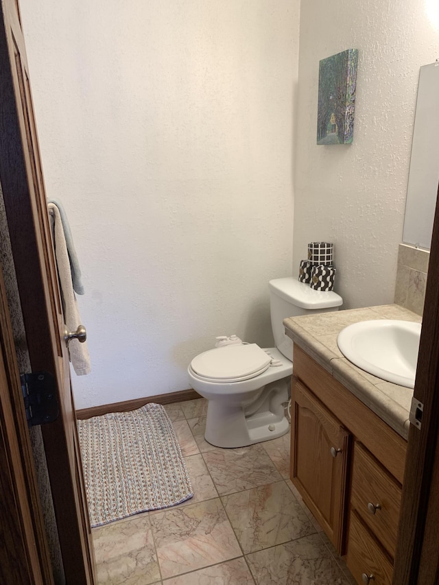 bathroom with baseboards, toilet, marble finish floor, and vanity