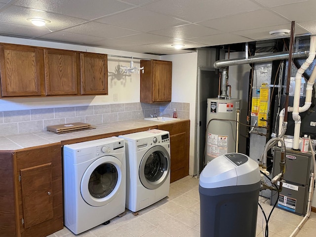 clothes washing area featuring a sink, washing machine and dryer, water heater, cabinet space, and light tile patterned floors