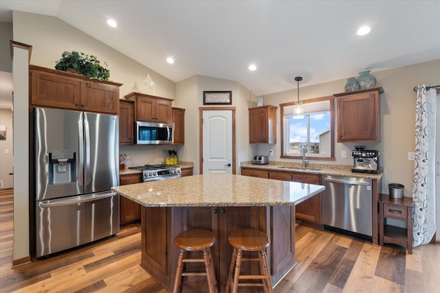 kitchen featuring a kitchen island, a sink, light wood-style floors, vaulted ceiling, and appliances with stainless steel finishes