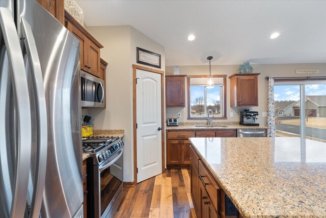 kitchen with appliances with stainless steel finishes, brown cabinets, wood finished floors, a sink, and a wealth of natural light