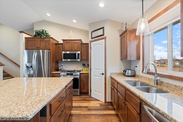 kitchen featuring light stone counters, wood finished floors, vaulted ceiling, stainless steel appliances, and a sink