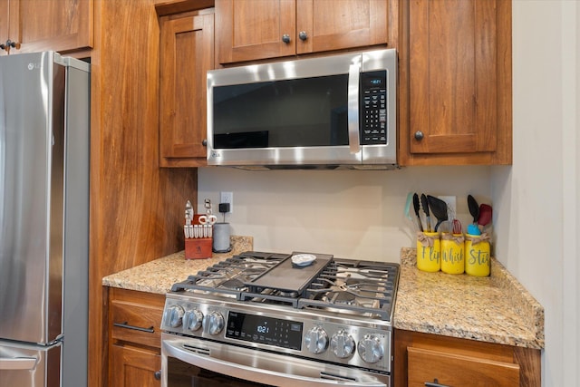 kitchen featuring stainless steel appliances, light stone countertops, and brown cabinets