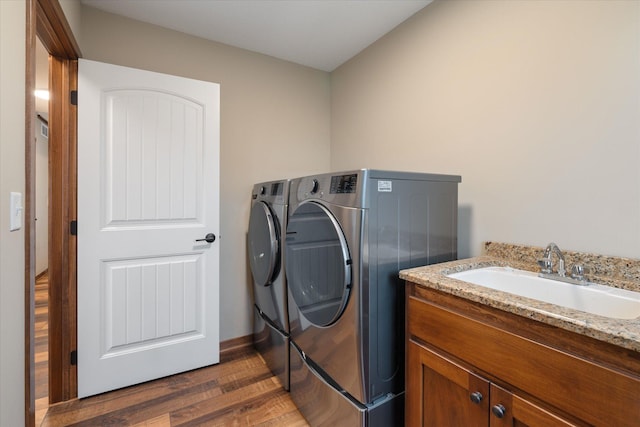 clothes washing area featuring cabinet space, baseboards, dark wood-style flooring, washing machine and clothes dryer, and a sink