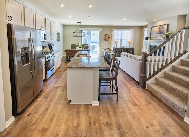 kitchen with a kitchen island with sink, stainless steel appliances, light stone countertops, a kitchen bar, and decorative light fixtures