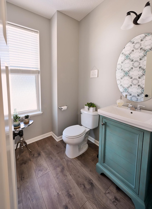 half bathroom featuring baseboards, vanity, toilet, and wood finished floors