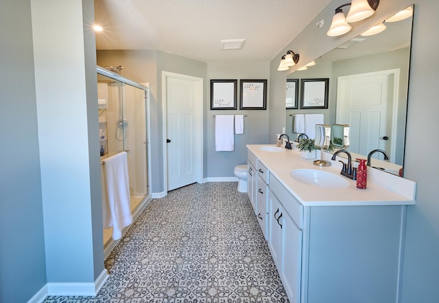 bathroom featuring double vanity, toilet, a stall shower, a sink, and baseboards