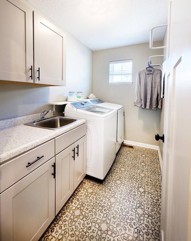 clothes washing area with washer and clothes dryer, cabinet space, a sink, a textured ceiling, and baseboards