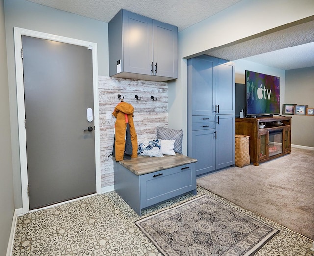 mudroom featuring a textured ceiling, baseboards, and light colored carpet