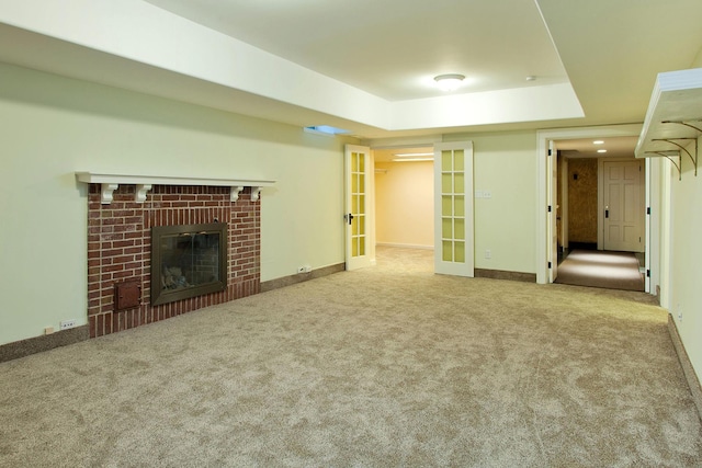 unfurnished living room with carpet floors, a fireplace, baseboards, french doors, and a tray ceiling