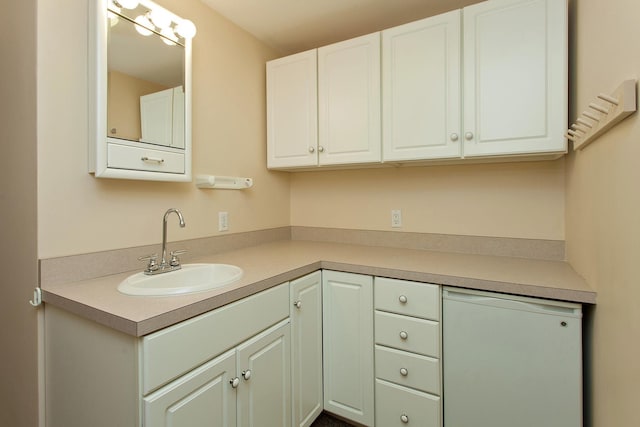 kitchen featuring fridge, white cabinetry, light countertops, and a sink