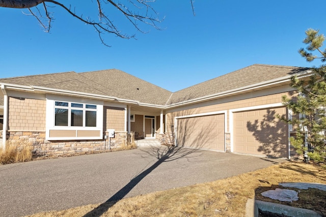 view of front facade with driveway, stone siding, a shingled roof, and a garage