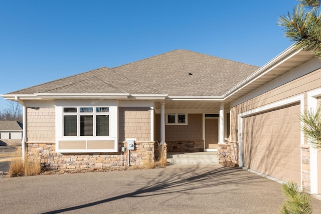 exterior space featuring a garage, stone siding, a shingled roof, and driveway