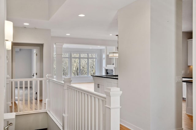 hallway featuring baseboards, wood finished floors, an upstairs landing, ornate columns, and recessed lighting