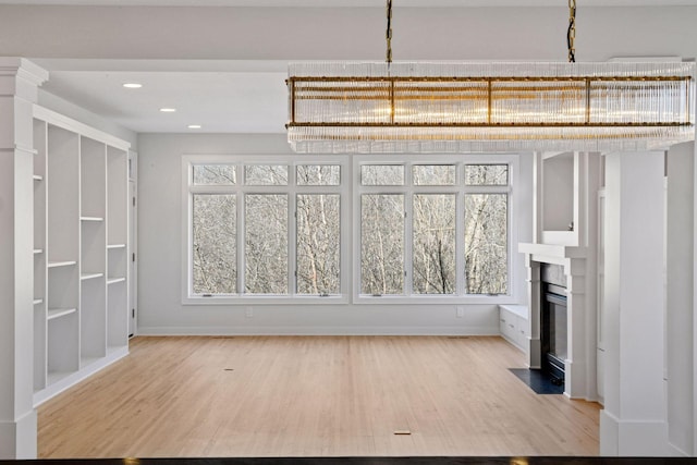 unfurnished dining area with a fireplace with flush hearth, light wood-type flooring, baseboards, and recessed lighting